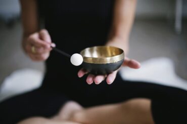 Image of female from shoulders down sat cross legged, wearing black workout gear holding a tibetan bowl