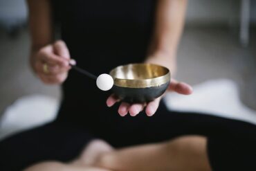 Image of female from shoulders down sat cross legged, wearing black workout gear holding a tibetan bowl