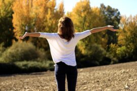 Back of dark haired lady with her arms outstretched breathing in the natural air outside helping to relieve her asthma