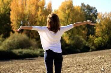 Back of dark haired lady with her arms outstretched breathing in the natural air outside helping to relieve her asthma