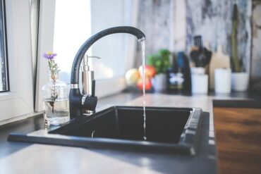 Black sink in a kitche n with middle black tap puring water into sink. Water filtration