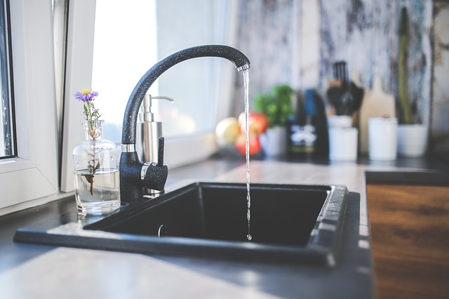 Black sink in a kitche n with middle black tap puring water into sink. Water filtration