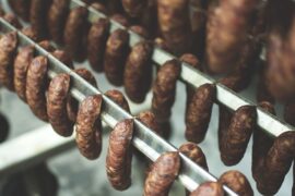 Three rows of smoked sausages hanging on smoking racks