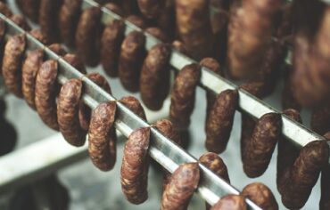 Three rows of smoked sausages hanging on smoking racks