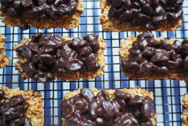 Close up of rectangular flapjack topped with dark chocolate raisins on a wire cooling rack with blue and white striped background