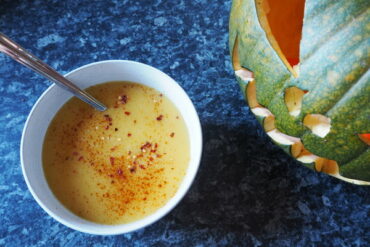 Boel of spicy pumpkin soup topped with chilli flakes next to a carved green jack o lantern