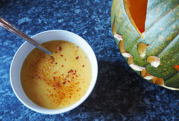 Boel of spicy pumpkin soup topped with chilli flakes next to a carved green jack o lantern