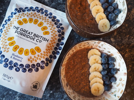 Packet of Blueberry & Banana The Great British Porridge Co. Porridge next to two bowls of porridge topped with sliced banana and blueberries