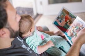 Dad looking at a picture book with a baby on his lap trying to establish a good bedtime routine