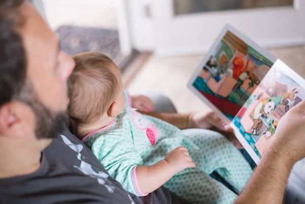 Dad looking at a picture book with a baby on his lap trying to establish a good bedtime routine