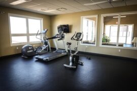 Three exercise machines positioned in the corner of an emoty fitness studio - a treadmill, exercise bike and cross trainer