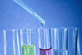 close up of 4 test tubes filled with different coloured fluid and a pipette dropping something into one of them