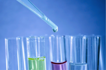 close up of 4 test tubes filled with different coloured fluid and a pipette dropping something into one of them