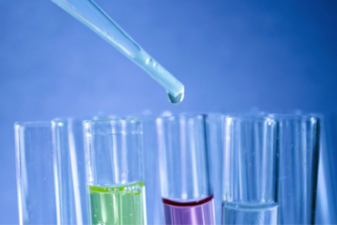 close up of 4 test tubes filled with different coloured fluid and a pipette dropping something into one of them