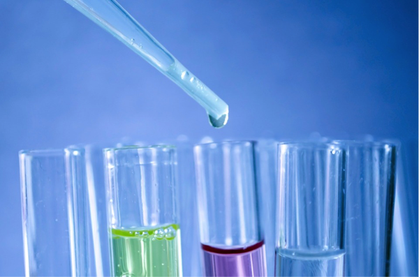 close up of 4 test tubes filled with different coloured fluid and a pipette dropping something into one of them