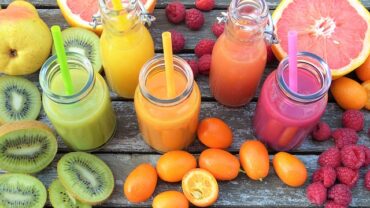 5 brightly covered smoothies in glass bottles with straws. surrounded by fresh fruits. rainbow food for detox
