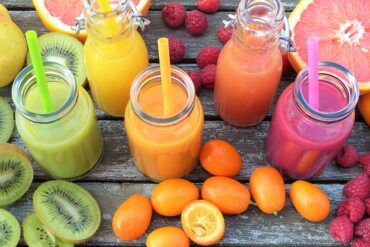 5 brightly covered smoothies in glass bottles with straws. surrounded by fresh fruits. rainbow food for detox