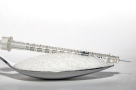 Close up of a teaspoon filled with sugar and in insulin injection is lying on top