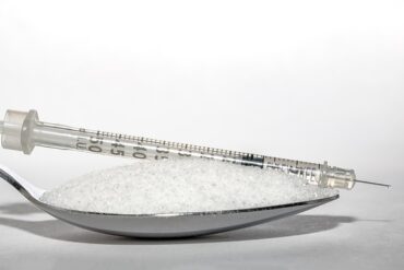 Close up of a teaspoon filled with sugar and in insulin injection is lying on top