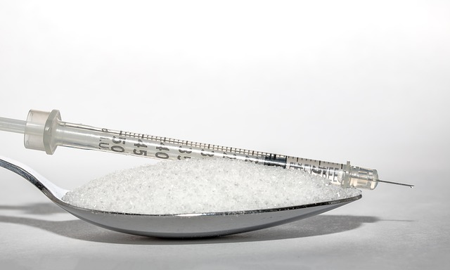 Close up of a teaspoon filled with sugar and in insulin injection is lying on top