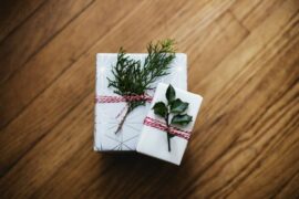 Two christmas presents stacked on top of one another. Wrapped in white natural paper and tied with a red patterned ribbon. here are evergreen leaves ticked in the ribbon.