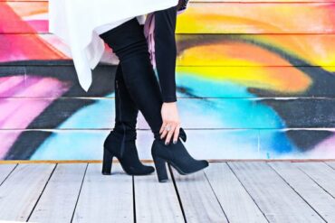 Woman's legs in black boots on a wooden floor against a graffiti background