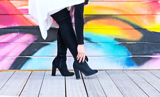 Woman's legs in black boots on a wooden floor against a graffiti background