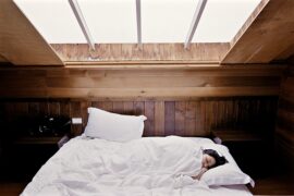 dark haired woman lying diagonally in bed with her head poking out of a white duvet