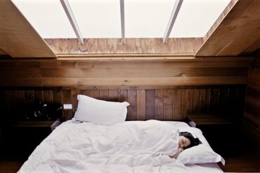 dark haired woman lying diagonally in bed with her head poking out of a white duvet