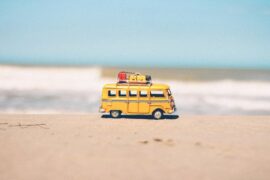 Child's camper van toy with mini luggage on it's roof on the sand with the sea in the background