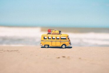 Child's camper van toy with mini luggage on it's roof on the sand with the sea in the background