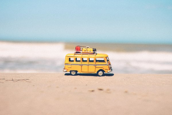 Child's camper van toy with mini luggage on it's roof on the sand with the sea in the background