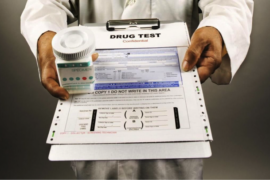 Close u up for a medical drug test form on a clipboard being held by a doctor who is also holding a jar of pills
