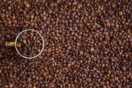 Background filled with coffee beans and a single cup is sat on top on the left hadn side, also filled with coffee beans