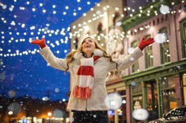 Blond haired woman stood outsode underneath Christmas firy lights.