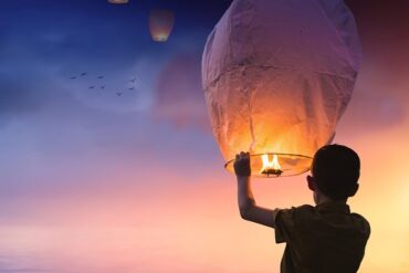 Silhouette of a boy holding a chinese lantern at new year waiting to release it with the other ones that are floating away at sunset