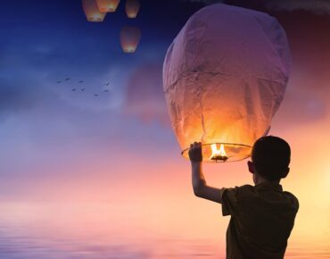 Silhouette of a boy holding a chinese lantern at new year waiting to release it with the other ones that are floating away at sunset