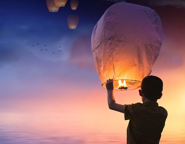Silhouette of a boy holding a chinese lantern at new year waiting to release it with the other ones that are floating away at sunset