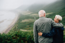senior citizen couple embracinf in front of a hillside beach and loving life