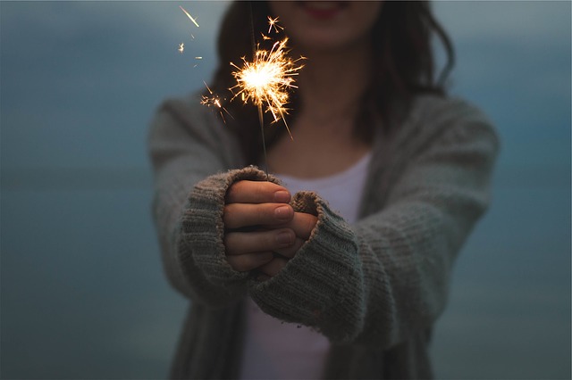 Brunette female holding a sparkling out in front of her. She is wearing a white top and a grey knitted cardigan and the photo is cut off so that you can only see her from the mouth down to her waist.