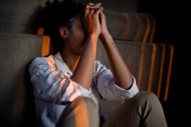 Yound black woman sat on the stairs with her elbows resting on her kness and her forehead resting against her hands. She looks as though she is depressed and needs help.