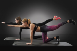 Two women exercising together set against a black background. They are on their knees with one lef stretched out behind them and the opposite arm stretched out in front of them.