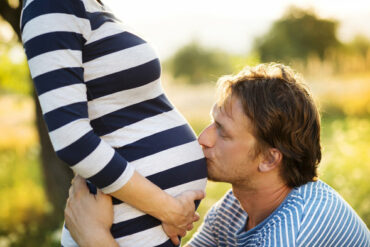 Man crouched down kissing his partner's pregnant belly.
