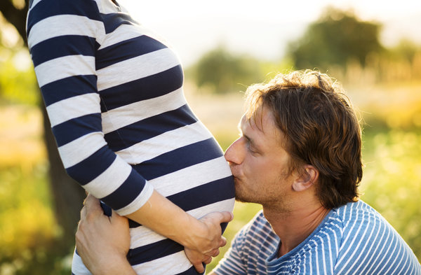 Man crouched down kissing his partner's pregnant belly.