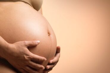 close up of a pregnant ladies bare belly with her hands cradling it.