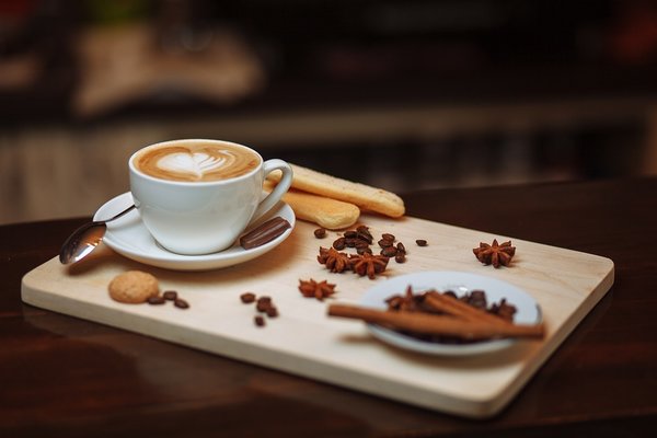 cappucino coffee in a white cup on a wooden board with scattered coffee beans and biscuits