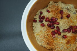 Close up of a bowl of smoked aubergine hummus garnished with pomegranate seeds and dusted with smoked paprika