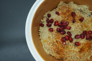 Close up of a bowl of smoked aubergine hummus garnished with pomegranate seeds and dusted with smoked paprika