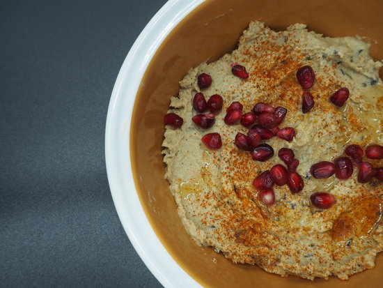 Close up of a bowl of smoked aubergine hummus garnished with pomegranate seeds and dusted with smoked paprika