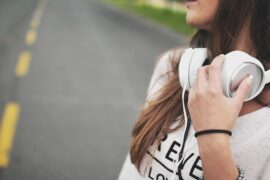 Close up of the side of a teenage girl with long dark hair and white headphones round her neck. there is a road in the back ground.